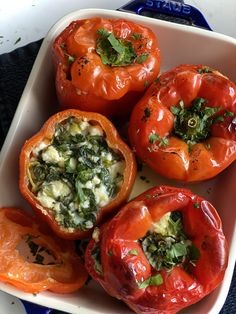 four stuffed red peppers in a white dish with herbs on the top and green stuff inside