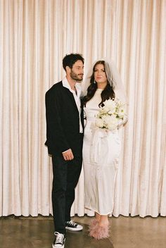 a bride and groom pose for a photo in front of the curtained backdrop at their wedding