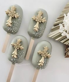 four chocolate covered lollipops decorated with gold crosses and pearls are on a white table