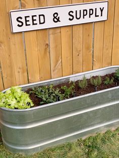 a metal container filled with plants next to a wooden fence and sign that says seed & supply