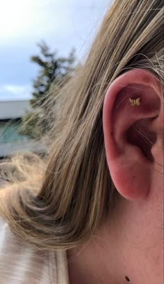 a close up of a person's ear with a small gold butterfly on it