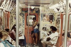 several people sitting on a subway car with graffiti all over the walls and flooring