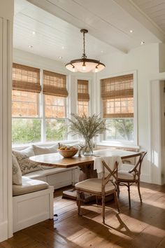 a table and chairs in a room next to windows with roman shades on the windowsills