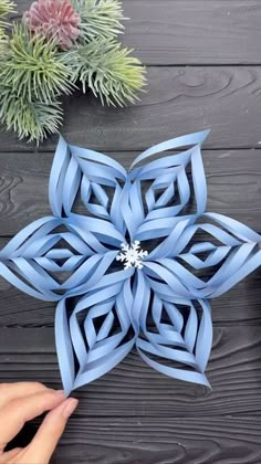 someone is making an origami snowflake out of blue paper on a wooden table