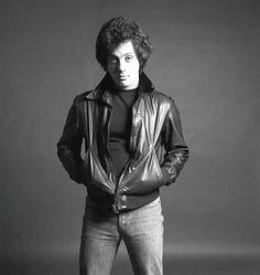 a black and white photo of a man in a leather jacket with his hands on his hips