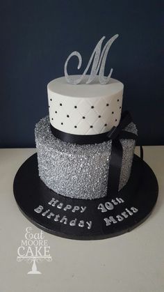 a black and silver birthday cake with the letter m on it's top tier