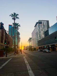 the sun is setting on an empty city street with palm trees in the foreground