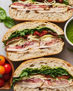 three sandwiches with meat, cheese and veggies next to some sauces on the table