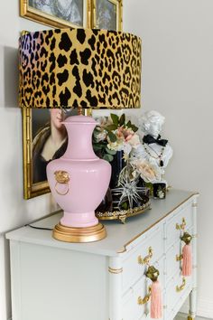 a pink vase sitting on top of a white dresser next to a framed photo and a leopard print lamp