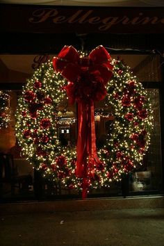 a christmas wreath with red bows and lights in front of a storefront at night