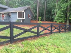 a black fence in front of a blue house with trees and grass on the lawn