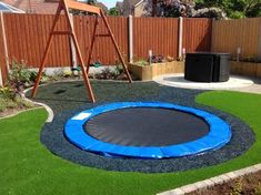 a backyard with artificial grass and a blue trampoline in the center, next to a wooden swing set