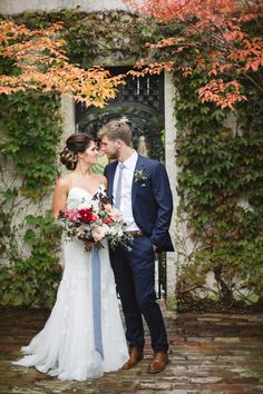 a bride and groom standing in front of an ivy - covered building with red flowers