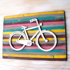 a wooden sign with a bicycle painted on it's side and multicolored stripes