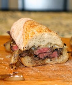 a sandwich with meat and onions on a cutting board