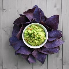 a white bowl filled with guacamole and purple chips