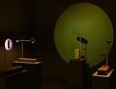 two lamps on pedestals in front of a green wall with a round light behind them