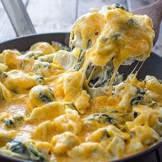 a spoon full of cheese and spinach being lifted from a skillet