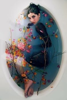 a woman sitting in a bathtub with flowers floating around