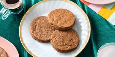 three cookies on a plate next to two cups of coffee