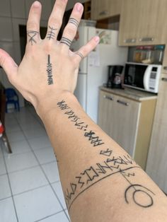 a person's hand with tattoos on it in a kitchen area next to a refrigerator