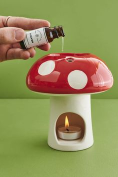 a person is pouring an oil into a mushroom shaped candle holder with a lit candle in it