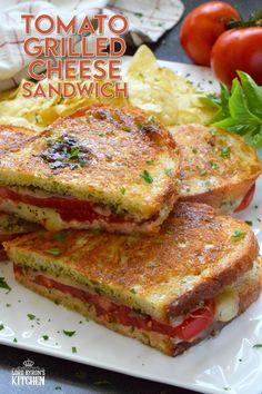 two grilled cheese sandwiches on a white plate with tomatoes and lettuce next to them