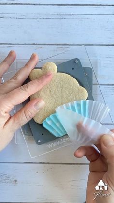 two hands are holding some cookies in plastic wrappers on a white wooden table with a person's hand reaching for one