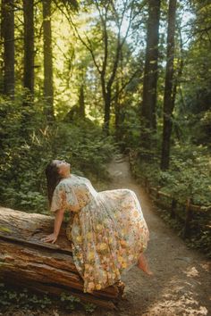 a woman in a floral dress sitting on a log in the middle of a forest