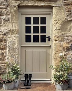 a pair of black rubber boots sitting in front of a stone building with two planters