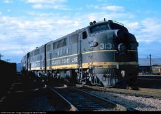 a train is traveling down the tracks under a blue sky with some clouds in the background