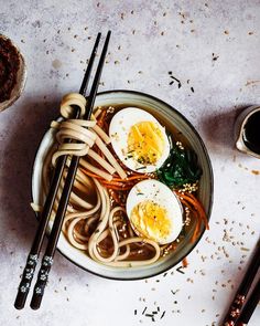 a bowl of noodles, eggs and chopsticks on a table with other food items