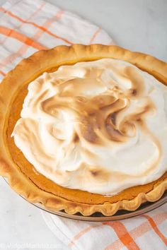 a pie with white frosting sitting on top of a checkered table cloth next to an orange and white napkin