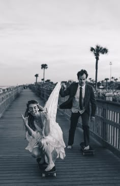 a man riding a skateboard next to a woman in a dress on a bridge