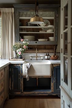 an old fashioned kitchen with blue cabinets and white dishes on the shelf above the sink