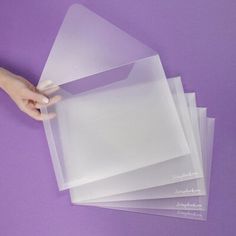 three clear envelopes are stacked on top of each other, one being held by a hand