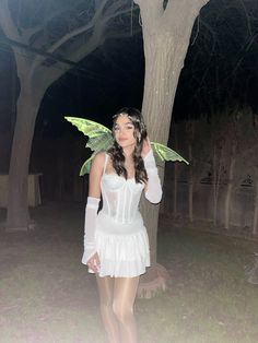 a woman dressed as a fairy standing in front of a tree with wings on her head