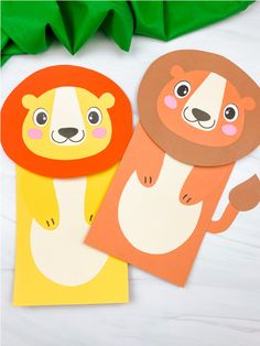 two paper animals are sitting next to each other on a white surface with green leaves in the background