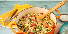 a pot filled with pasta and vegetables on top of a wooden table next to rice