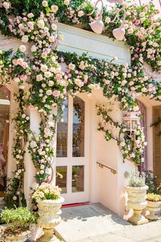 the entrance to a flower shop with pink and white flowers growing on it's walls