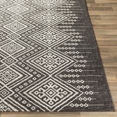 a black and white area rug with an intricate design on the bottom, along with wooden flooring