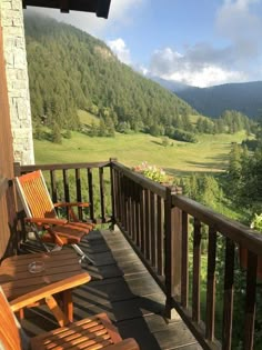 two wooden chairs sitting on top of a porch next to a lush green hillside covered in trees