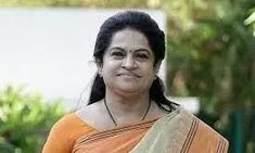 a woman in an orange and white sari is standing outside with trees behind her