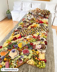 a long table filled with lots of food on top of a wooden floor next to a white couch