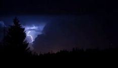 a lightning bolt is seen in the dark sky above some trees and pine trees at night