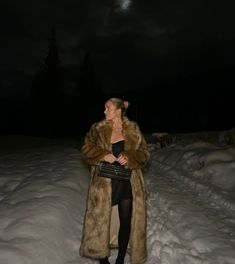 a woman standing in the snow at night with her hand on her hip wearing a fur coat