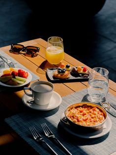 a table topped with plates and bowls of food next to glasses on top of a wooden table