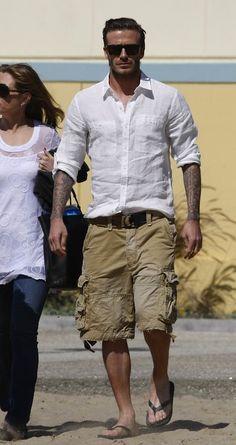 David Beckham was spotted filming a Diet Pepsi commercial out on the beach in Santa Monica, CA. Kicking around a soccer ball while having a Pepsi in hand, David was seen in a pair of Mosley Tribes sunglasses ($180), a white long-sleeve linen button down shirt, and Abercrombie & Fitch Algonquin light wash cargo shorts ($60). David Beckham Style, Shorts Fashion, Cargo Shorts Men, Gym Style, David Beckham, Mens Casual Outfits, Men Looks, Mens Summer