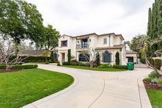 a large white house with lots of trees in the front yard and landscaping around it