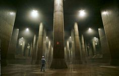 a man standing in the middle of an empty room with columns and lights on either side